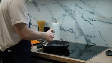 Mutfak sahnesi, indüksiyon tenceresinde bir tavanın titizlikle hazırlandığını vurguluyor. Becerikli şef yemek yapmaya hazırlanıyor, tavaya yağlı yağ ekliyor.