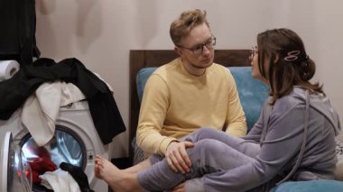 Çift sıcak bir ortamda oturur, derin bir sohbete dalarlar. Arka plandaki bitmemiş çamaşırlar günlük yaşamlarını vurguluyor ve güçlü duygusal bağlarını vurguluyor.