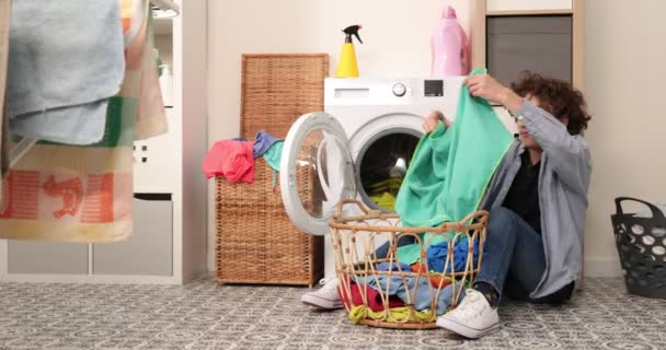 汚れた服を洗う 服の匂いが悪い 男の子は汚れた服を嗅ぎ 嫌悪感で洗濯機にそれらをスローします — ストック動画