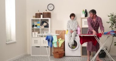 Aile, baba ve oğul çamaşır odasındaki ütü masasında ütü giysileri Aile aktiviteleri, ev işleri, çamaşır yıkama ve temizlik konsepti