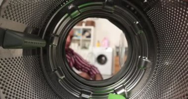 Çamaşır makinesinin içinden bakınca, adamın biri çamaşır makinesine renkli bir çamaşır koyuyor..