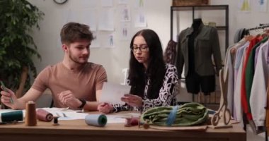 Moda tasarımcılarının ve terzilerin işi. Moda tasarımcıları stüdyolarında çalışıyor. Renkli Kumaşlar, Giysiler Asılma ve Dikiş Ögeleri Görünür