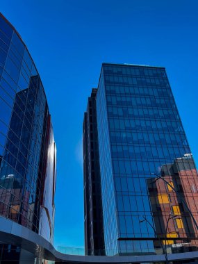 Modern cam gökdelenler şehir manzarasında mavi gökyüzünü yansıtıyor