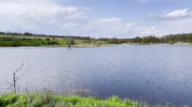 Bulutlu gökyüzü ile sakin göle bahar yağmuru yağıyor