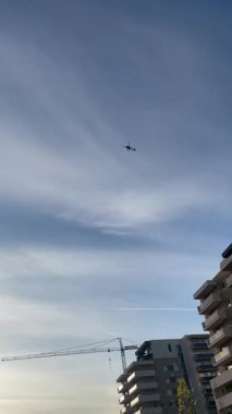 Helikopter inşaat vinciyle şehrin üzerinde uçuyor.