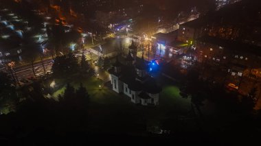 Şehir sokakları ve aydınlık binalarla çevrili bir kilisenin gece hava görüntüsü