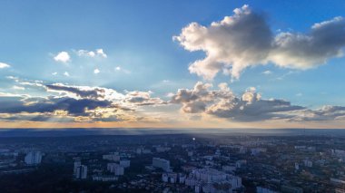 Gün batımında dramatik bulutları aşan güneş ışınlarıyla dolu bir şehir manzarası.