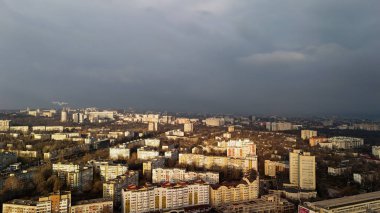 Altın güneş ışığı ve kara fırtına bulutlarıyla dolu havadan bir şehir.