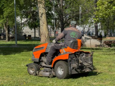 Parkta çim biçme makinesinde çalışan kişi