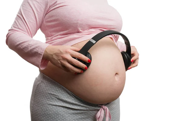 妊娠中の女性のクローズアップは 音楽愛好家の概念として白い背景に隔離された腹にヘッドフォンを保持 — ストック写真