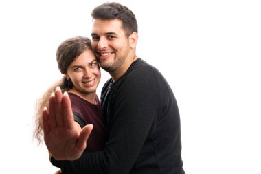 Cute smiling female model making stop stay away gesture using palm while hugging male boyfriend as romantic couple relationship concept isolated on white background