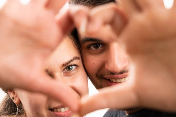 Selective focus close-up of cute male and female couple through heart symbol made with fingers as romantic concept isolated on white studio background