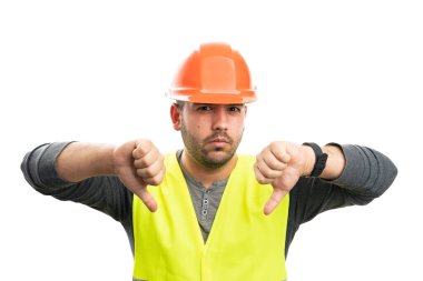 Miğfer ve floresan yelek giyen kızgın yetişkin bir müteahhit beyaz arka planda izole edilmiş, iki kez baş parmağından nefret eden bir jest yapıyor.