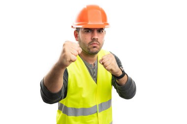 Kızgın erkek müteahhit iş üniforması giyiyor. Turuncu güvenlik kasketi ve sarı yelek. Yumruklarını dövüşürken gösteriyor.
