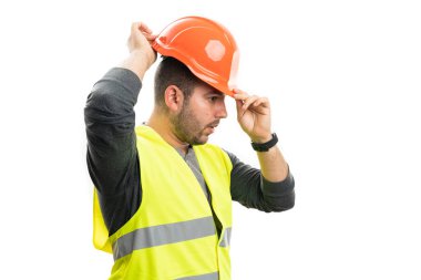 Yetişkin erkek müteahhit, beyaz arka planda izole edilmiş floresan yelek giyip turuncu güvenlik kaskını düzenlemeye hazırlanıyor.