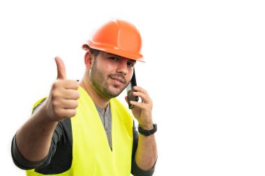 Güvenlik kaskı ve floresan yelek giyen gülümseyen erkek müteahhit telefonda konuşuyor. Beyaz arka planda izole edilmiş boş bir telif alanı gibi hareket ediyor.