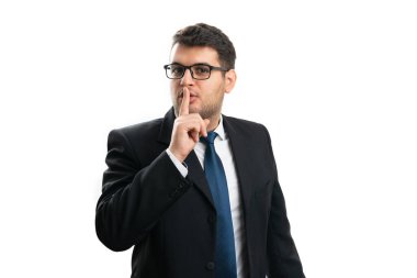 Ciddi bir ifadeye sahip yetişkin işadamı şık bir takım elbise ve ağzı kaplayan gözlük takıyor işaret parmağı kullanarak beyaz arka planda izole edilmiş gizli şşş hareketi yapıyor.
