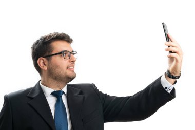 Yetişkin işadamı ofis kıyafeti, gözlük ya da gözlük takıyor. Beyaz stüdyo arka planında izole edilmiş akıllı telefon kullanarak selfie çekerken gülümsüyor.