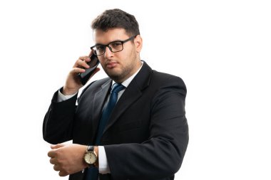 Zeki takım elbiseli ve gözlüklü ciddi iş adamı telefon görüşmesinde kol saatini beyaz arka planda izole edilmiş zaman tutma kurumsal konsepti olarak gösteriyor.