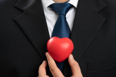 Kırmızı kalbin, beyaz arka planda izole edilmiş bir şirket konsepti olarak şık giyinen yetişkin iş adamlarının aşk sembolü olarak yakın plan görüntüsü.