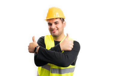 Koruyucu başlık takmış, gülümseyen erkek müteahhit beyaz arka planda izole edilmiş bir jest gibi iki başparmak işareti yapıyor.