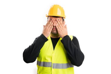 Sarı güvenlik kaskı ve floresan iş yeleği giyen erkek müteahhit beyaz stüdyo arka planında izole edilmiş gizli bir kavram olarak palmiyelerle gözlerini kapatıyor.