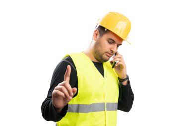 Flüoresan yelek giyen ve sarı kasketli meşgul bir erkek inşaat işçisi telefonda konuşurken işaret parmağı beyaza izole edilmiş bir şekilde bekliyor.
