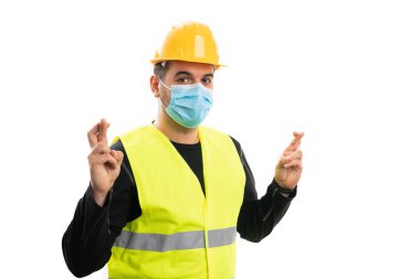 İş üniformalı, sarı kasketli, tıbbi ya da cerrahi maske takan erkek inşaat işçisi. İyi şanslar diliyor.