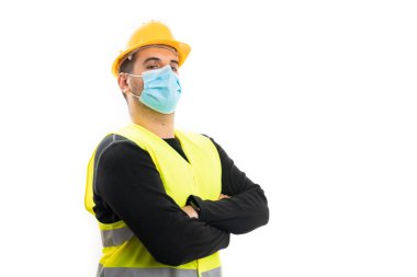 İş kıyafetleri içindeki erkek müteahhitin portresi kollarını çapraz tutuyor koruyucu bir tıbbi tek kullanımlık maske takıyor ve beyaz arka planda boş bir kopya alanı var.