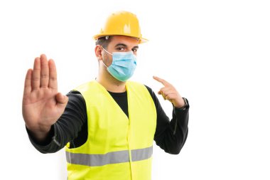 Yetişkin müteahhit, floresan yelek ve sarı koruyucu başlık takıyor. Parmağını cerrahi ya da tıbbi maskeye doğrultuyor. Palmiye hareketini, beyaz üzerine izole edilmiş kovid19 salgın konsepti olarak durduruyor.