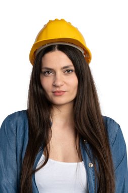 Sarı güvenlik kaskı, kot gömlek ve beyaz atlet giyen genç bir inşaat işçisinin yakın plan portresi. Kendine güvenen ve profesyonel bir ifadeyle doğrudan kameraya bakıyor. Beyaz bir arkaplanda izole edilmiş