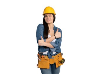 Kot gömlekli, beyaz kolsuz tişörtlü, gülümseyen bir kadın inşaat işçisi ve alet kemeri kollarını kavuştururken kendinden emin bir şekilde onay veriyor. Sarı güvenlik kaskı takıyor. Yetenekli ticaretlerde profesyonelliği ve pozitifliği simgeliyor. İzole bir şekilde...