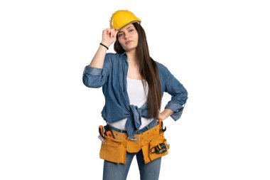 Sarı bir şapka ve alet kemeri takan kendine güvenen bir kadın inşaat işçisi doğrudan kameraya bakarken kaskını ayarlıyor. Kot gömlek ve kot pantolon giyer, profesyonellik ve hazırlık yayar, bu imajı temalar için ideal kılar.