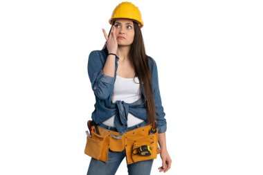 Sarı bir şapka ve alet kemeri takan genç bir inşaat işçisi tek eliyle yüzünü siliyor. Kot gömlek ve kot pantolon giyiyor, beyaz bir arka plana karşı yorgun ve düşünceli bir görünüm sergiliyor..