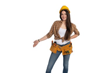 Ekose gömlekli ve alet kemerli mutlu bir kadın inşaat işçisi kolunu uzatarak bir jest yapıyor. Beyaz tenli, iş gücü, inşaat ve profesyonel temalar için ideal.