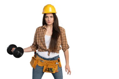 Sarı bir şapka ve alet kemeri takan kadın bir inşaat işçisi, fiziksel talepte bulunan güç, güç ve dayanıklılığı sembolize eden bir halteri kendinden emin bir şekilde kaldırır.
