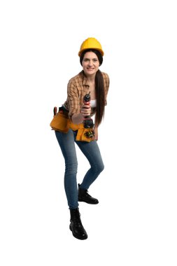 Güvenilir kadın inşaat işçisi elinde kablosuz matkapla öne doğru geliyor. Alet kemeri ve iş kıyafeti giyiyor..