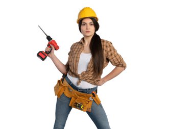 Sarı bir şapka ve alet kemeri takan kararlı bir kadın inşaat işçisi, beyaz arka planda dikilirken güvenli bir şekilde matkap tutuyor..