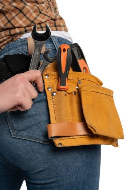 Kadın bir inşaat işçisinin eli, gerekli aletlerle dolu, günlük kot pantolon ve ekose gömlek giyen deri bir kemerin yanında iki metal anahtarı tutarken çekilmiş detaylı bir yakın plan..