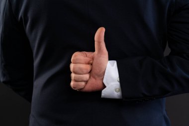 Bir adamın elinin resmi iş kıyafetleri içinde arkasından olumlu bir jest yapması gizli bir onay ya da ince bir ironi olduğunu gösteriyor..