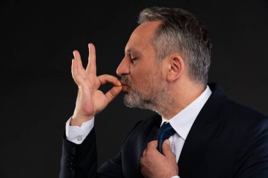 Olgun bir iş adamının yan görüntüsü şeflerin öpüşme hareketlerini gözleri kapalı yapıyor, profesyonel bir ortamda mükemmelliğini veya memnuniyetini ifade ediyor..