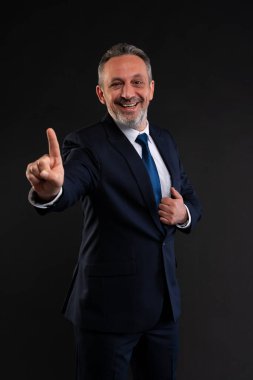 Takım elbiseli, kendine güvenen, gülümseyen ve tek parmağıyla işaret eden yetişkin bir iş adamı. Odaklanma, yön, liderlik ya da profesyonel bir ortamda hareket çağrısı öneriyor..