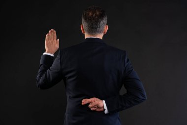 İş elbiseli bir adam arkadan görüldü. Ellerini kaldırarak yemin ederken arkasından iş çeviriyor. Sahtekarlığı ya da sahte vaatleri simgeliyor..