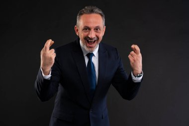 Takım elbiseli neşeli iş adamı ellerini kaldırmış, parmaklarını çapraz yapıp heyecanını ve umutlarını dile getiriyor..