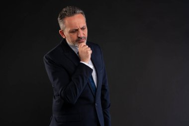 Takım elbiseli olgun bir işadamı, elleri çenesinde, derin bir şekilde düşüncelerini ve karar verme yetilerini ifade ediyor..