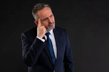 Takım elbiseli olgun işadamı şakağını işaret ederek eleştirel düşünce, strateji ve zekasını ifade ediyor..