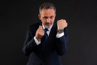 Takım elbiseli ciddi bir işadamı uluslararası para el hareketi yaparken aynı zamanda lüks bir kol saati sergiliyor, zenginliği ve zaman değerini simgeliyor..