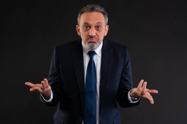 Takım elbiseli orta yaşlı bir adam, kafası karışmış bir yüz ifadesi takınıyor, omuz silkiyor, belirsizliğini dile getiriyor ya da bilmiyor..