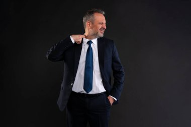 Takım elbiseli bir iş adamı gömleğinin yakasını çekiyor, rahatsız ve terli görünüyor. Sıcaklık, stres ya da baskı kavramı. Stüdyo çekimi koyu arkaplanda