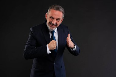 Takım elbiseli kendine güvenen işadamı yumruğunu sıkıyor ve kararlı bir ifadeyle avucuna vuruyor. Harekete ya da azme hazır olduğunu gösteriyor. Stüdyo çekimi.